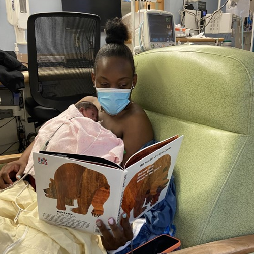 A mother in HUP’s intensive care nursery holds her baby to her bare chest under a pink blanket and reads the children’s book Brown Bear, Brown Bear, What Do You See?